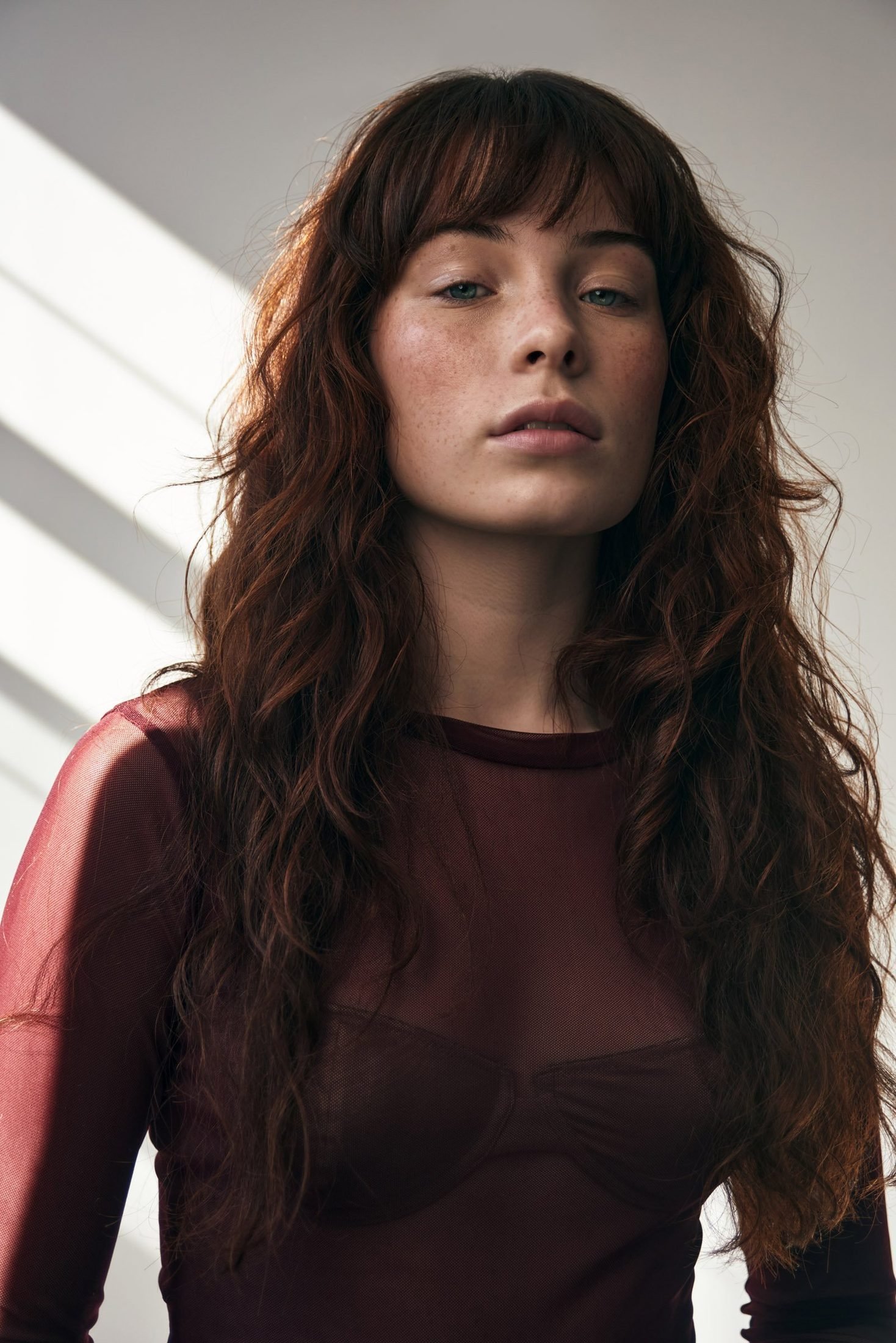 Natural light portrait of a red-haired woman beside window blinds