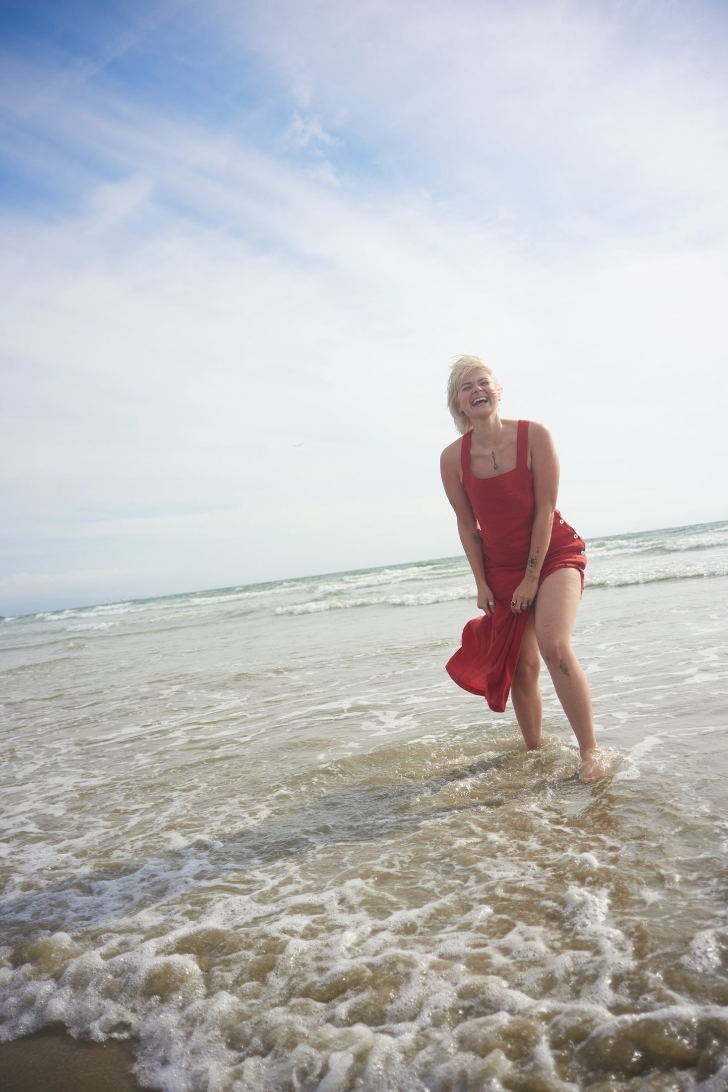 Joyful location portrait of a woman in a red dress standing in shallow ocean water