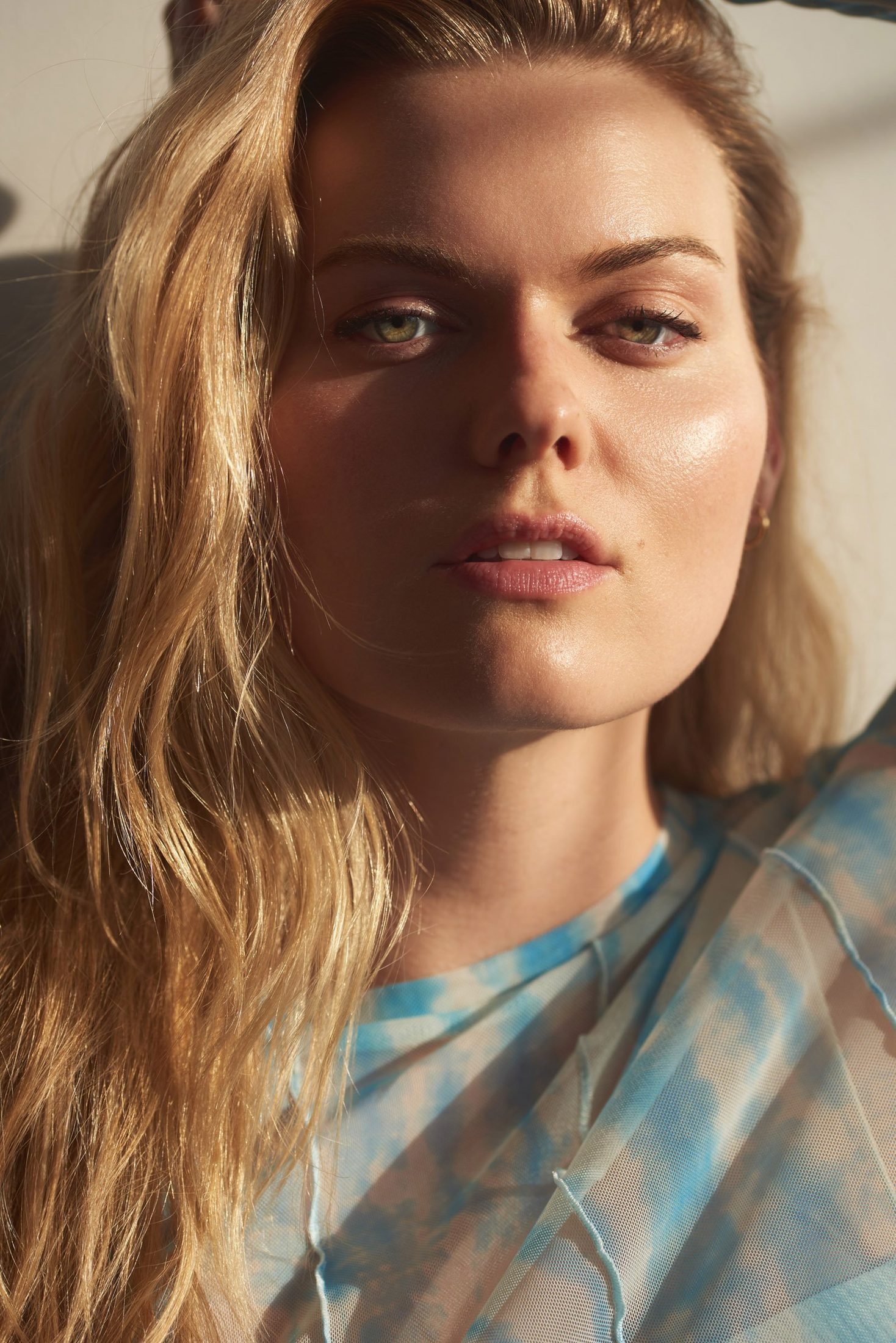 Beauty portrait of a blonde woman in a sheer blue-patterned top, partly in shadow