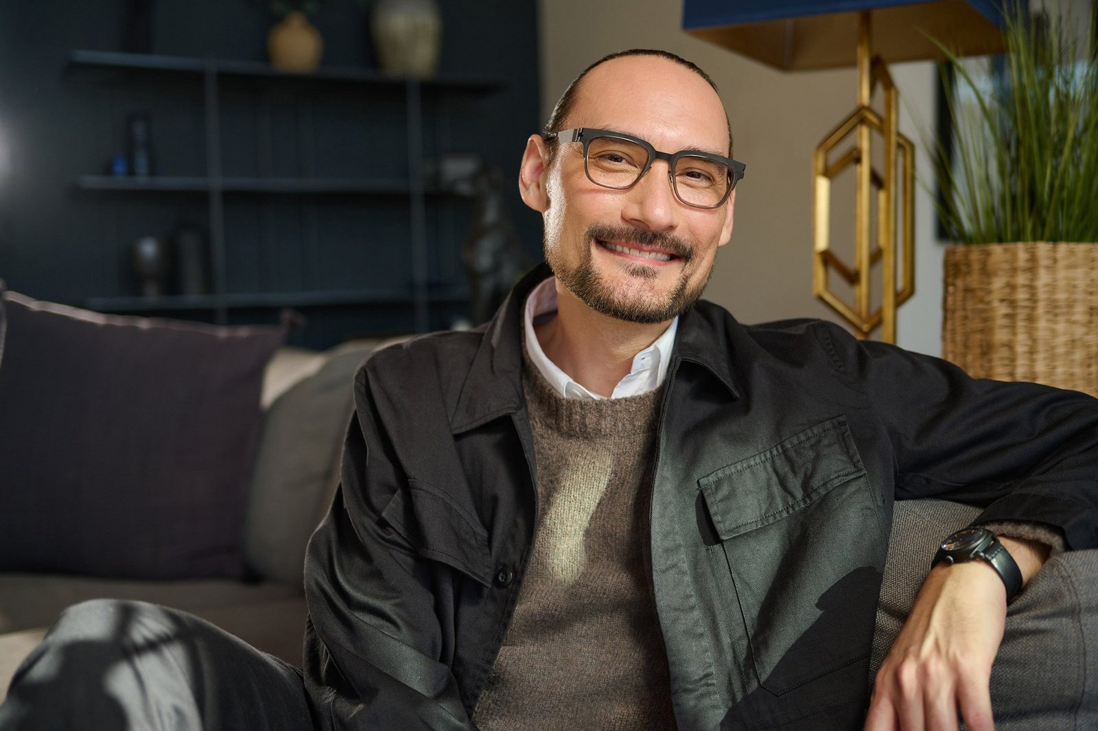 Relaxed business portrait of a smiling man with glasses on a beige couch