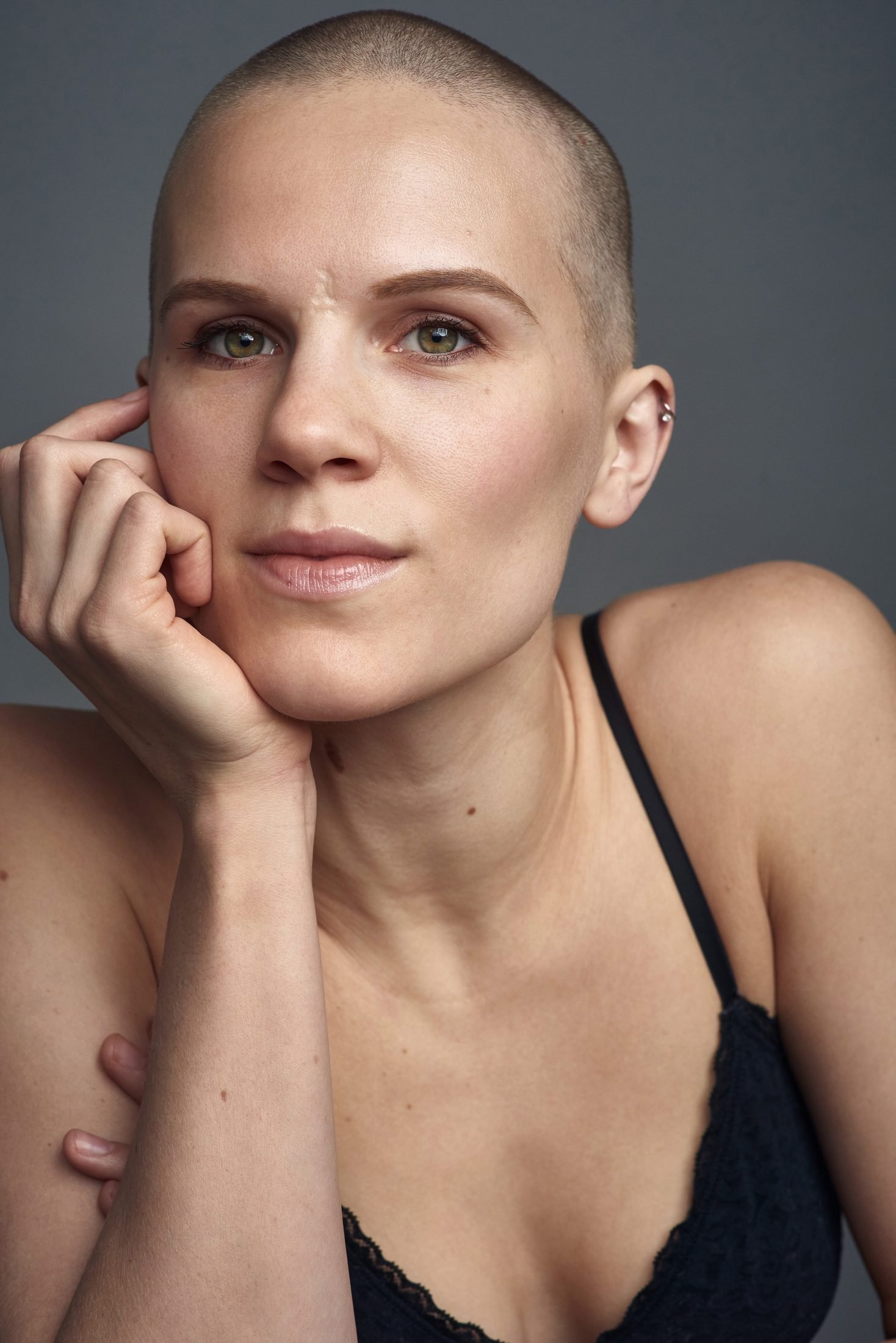 Studio portrait of a woman with a shaved head in a black lace top on grey