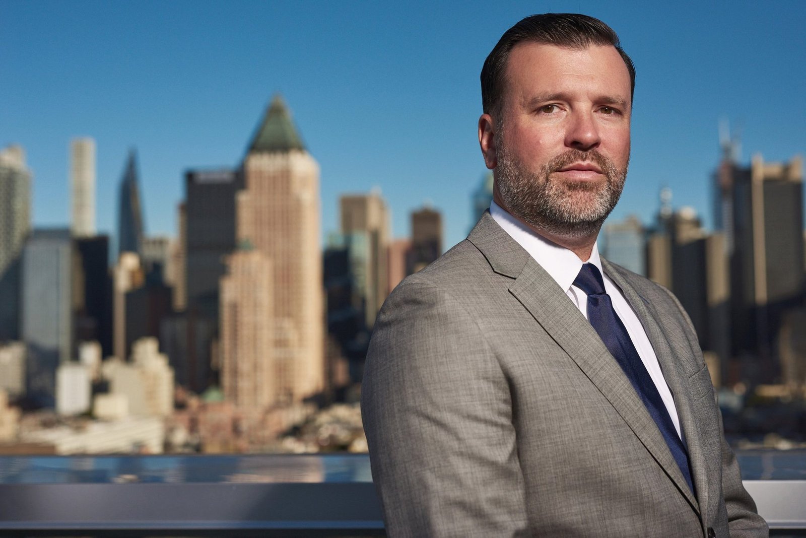 Corporate headshot of a man in a grey suit and blue tie on a rooftop