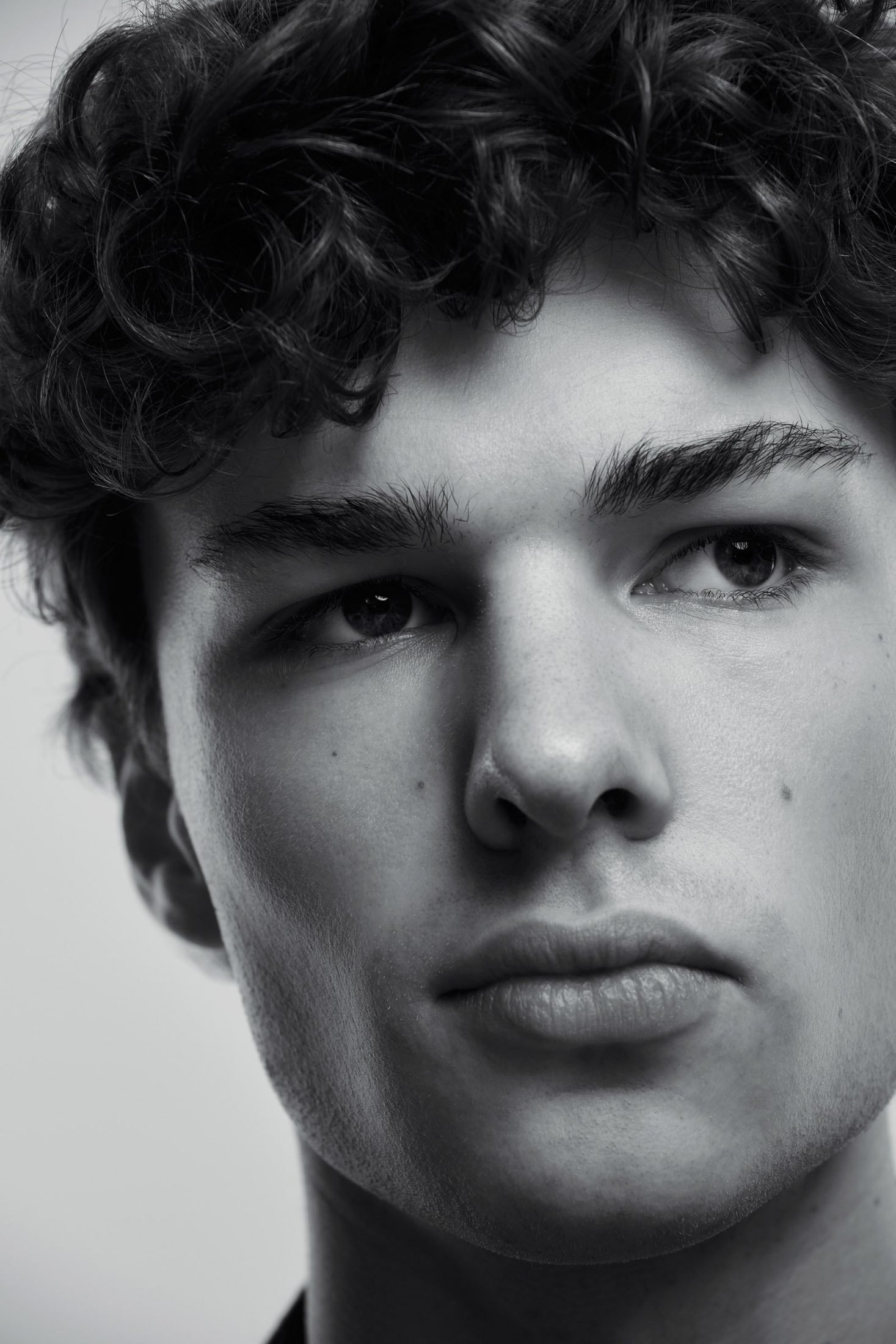 Black and white close-up actor headshot of a young man with curly hair