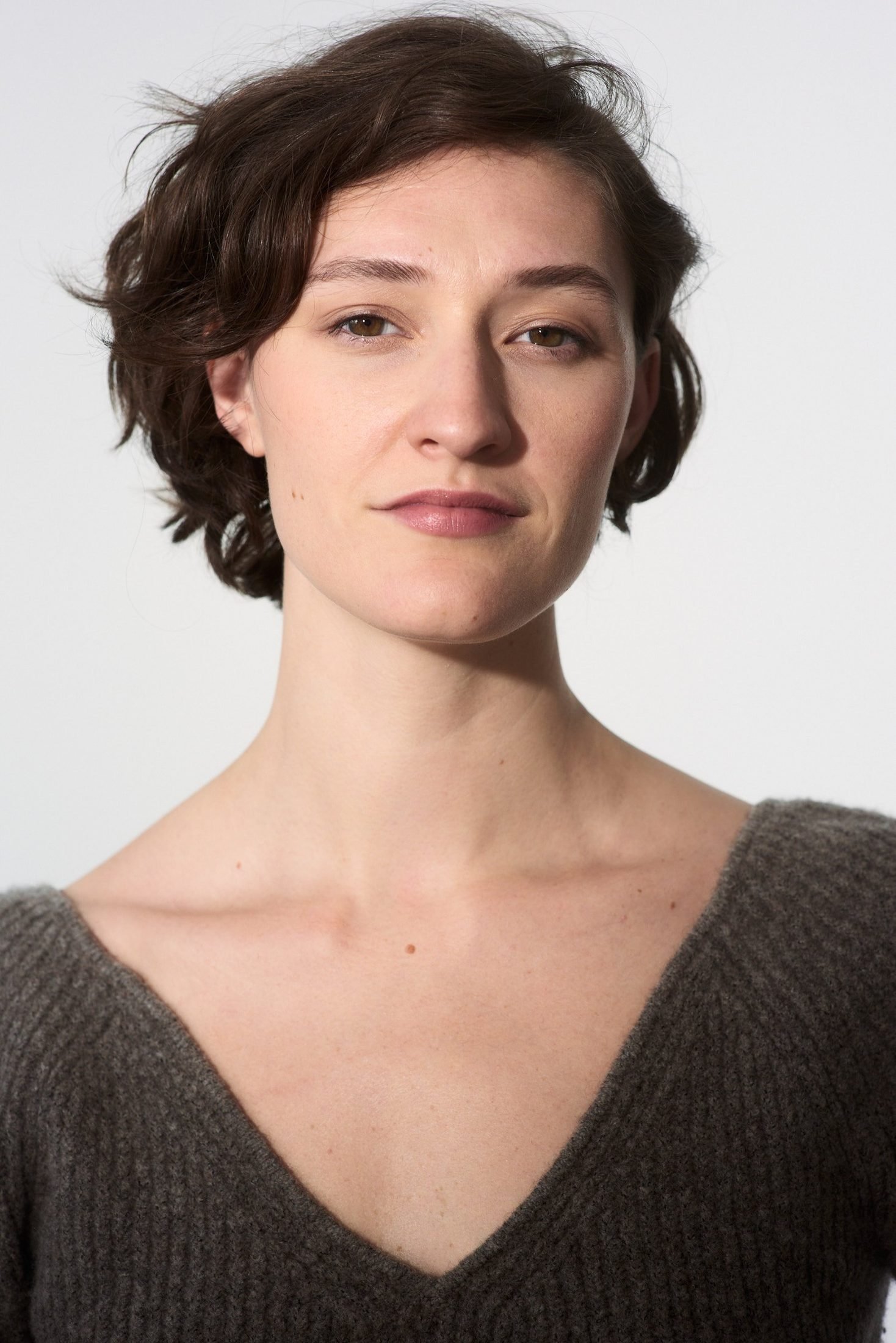 Clean studio headshot of a woman in a grey V-neck sweater on white