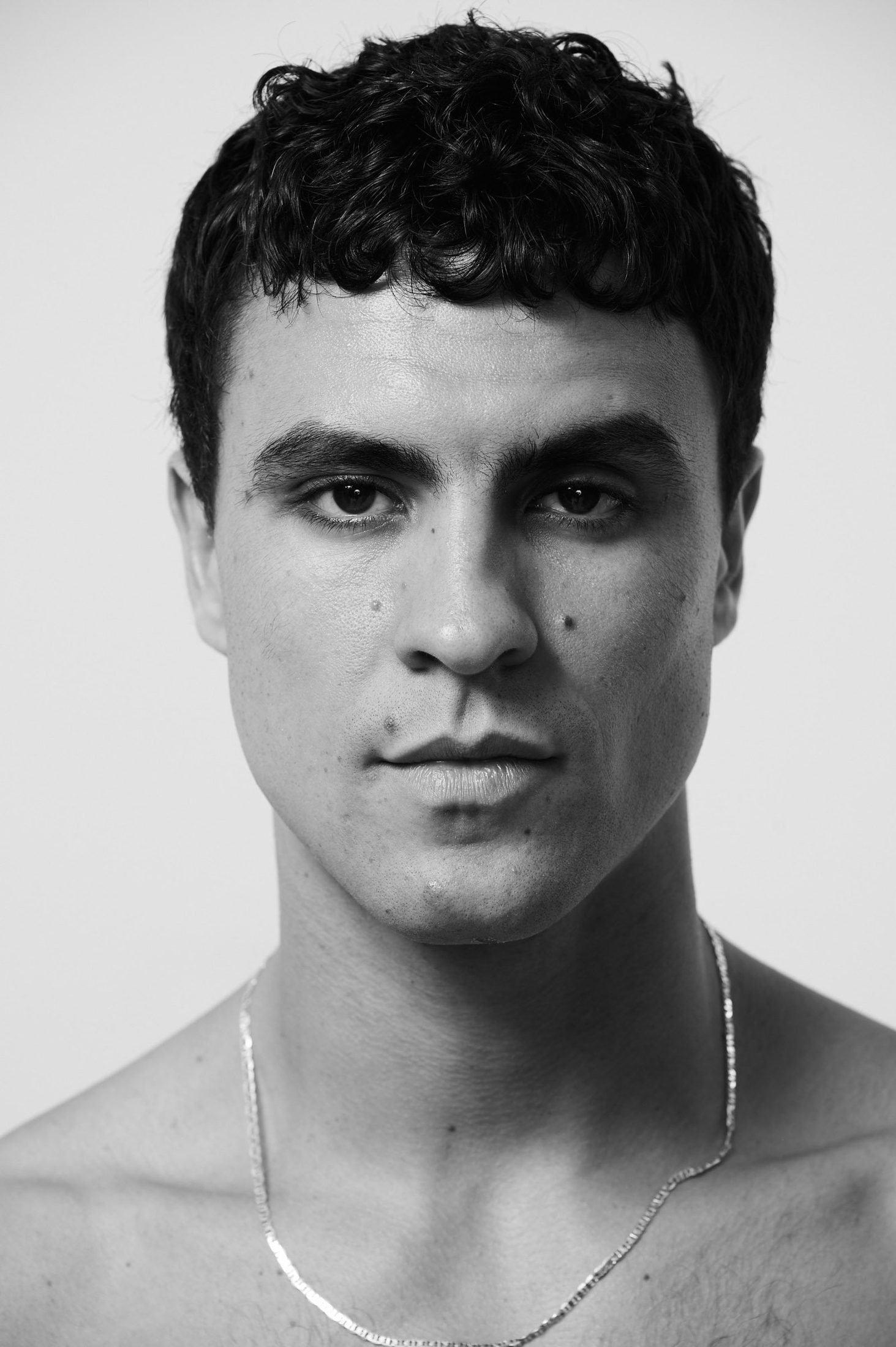 Black and white portrait of a young man with short curly hair and a necklace