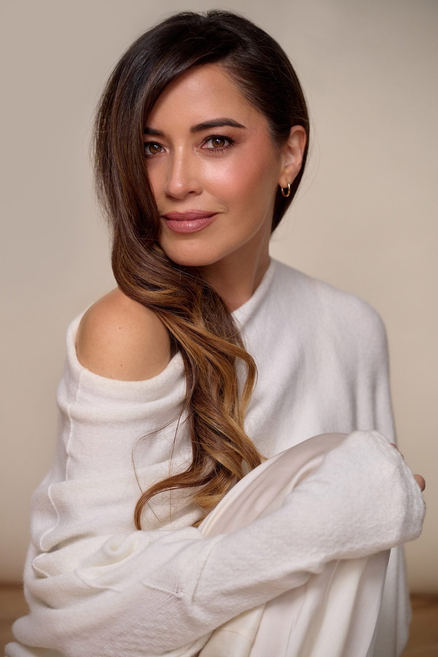Portrait of a woman with long wavy hair in a white off-shoulder sweater