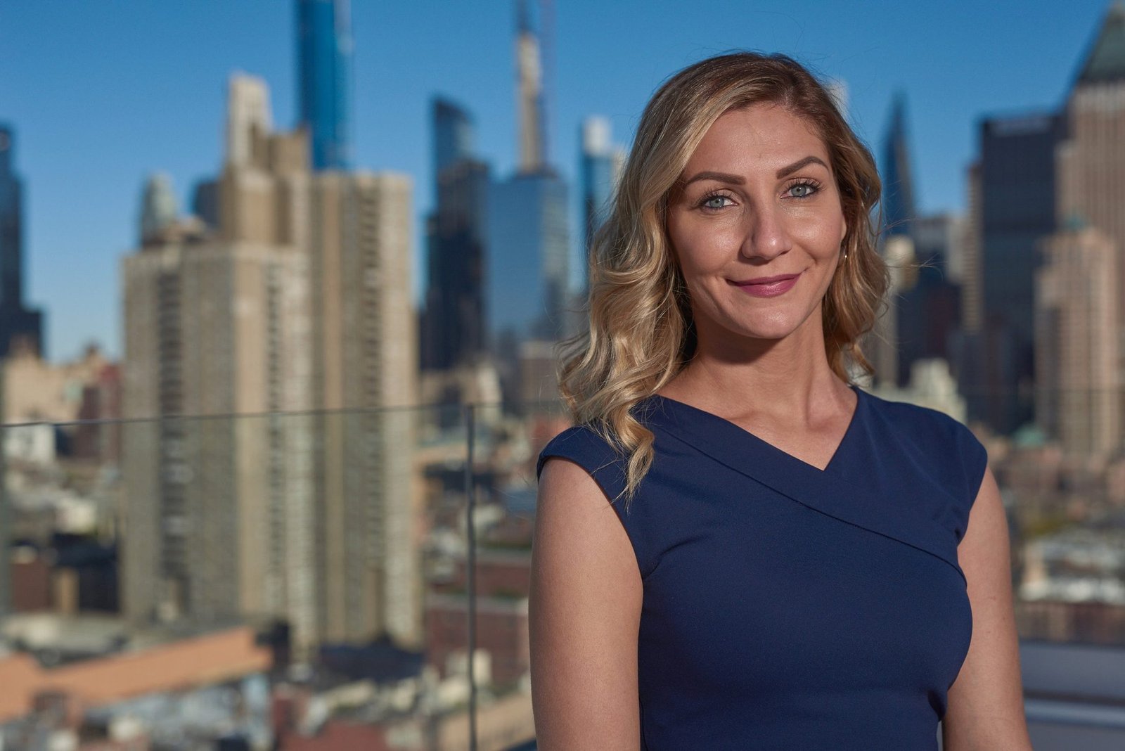 Outdoor corporate headshot of a woman in a blue top with a city skyline behind