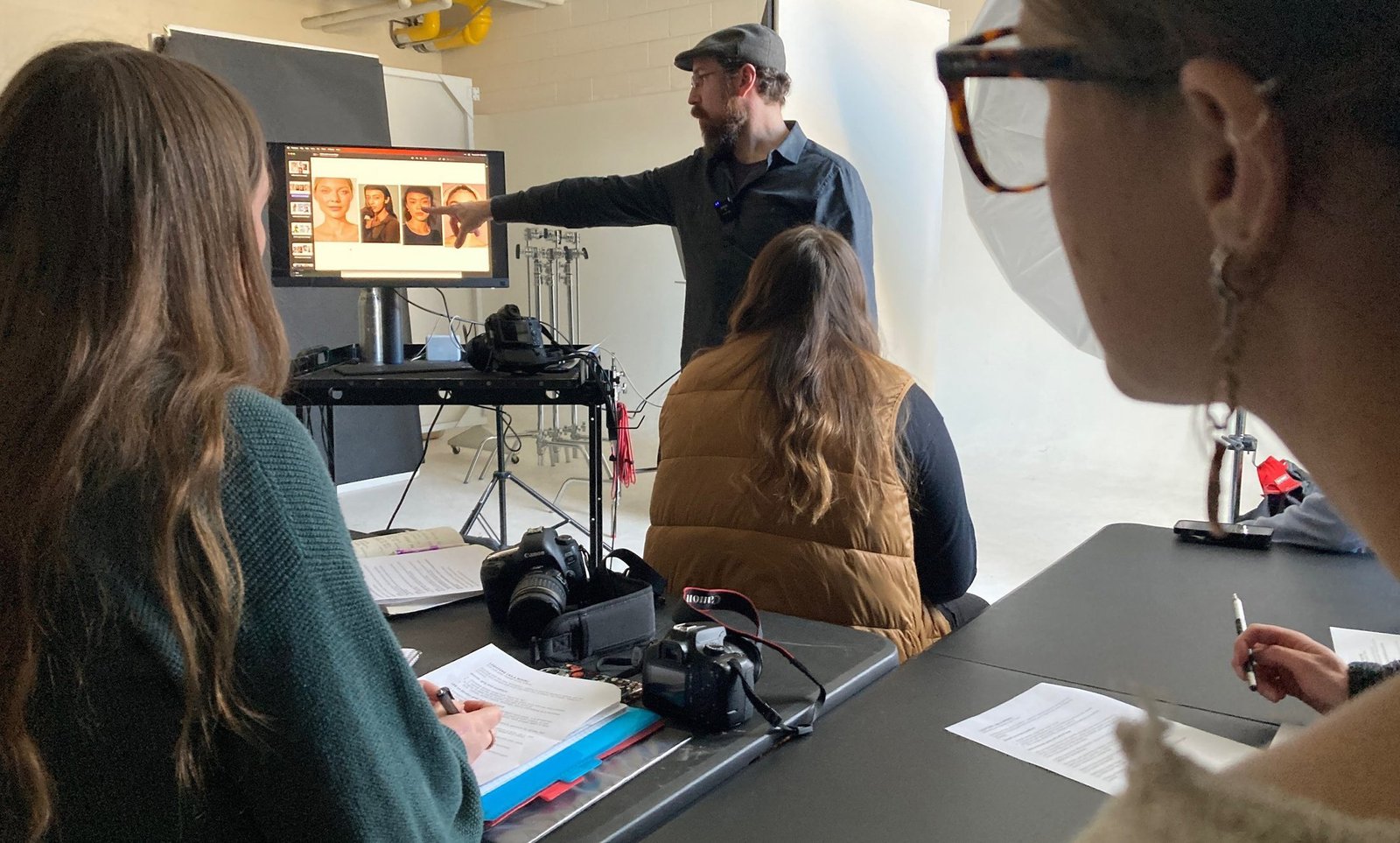 Photography students watching an instructor review portraits on a studio monitor